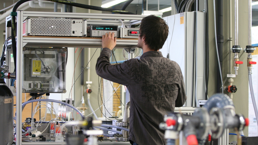 Foto einer Person in Rückansicht in einem Labor mit elektronischen Gerätschaften